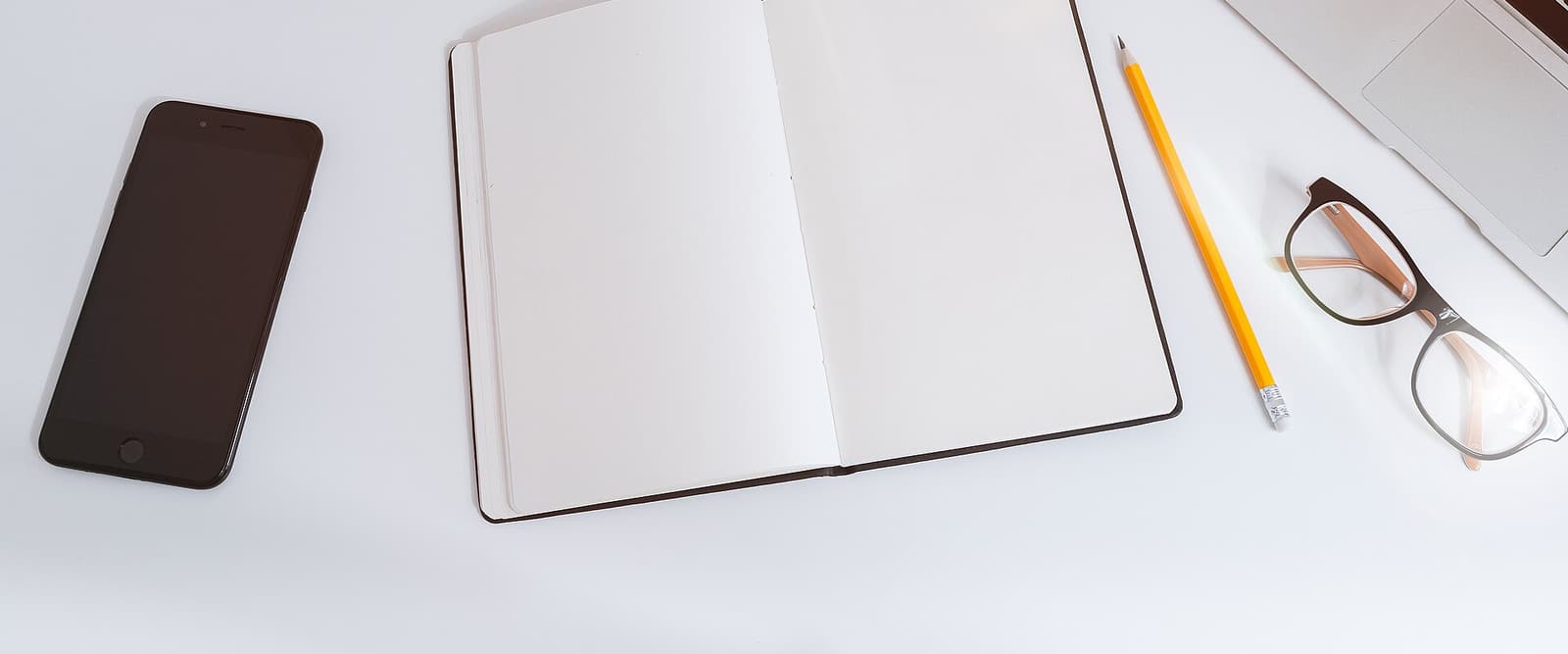 Notizbuch, Stift und Laptop auf einem weißen Tisch