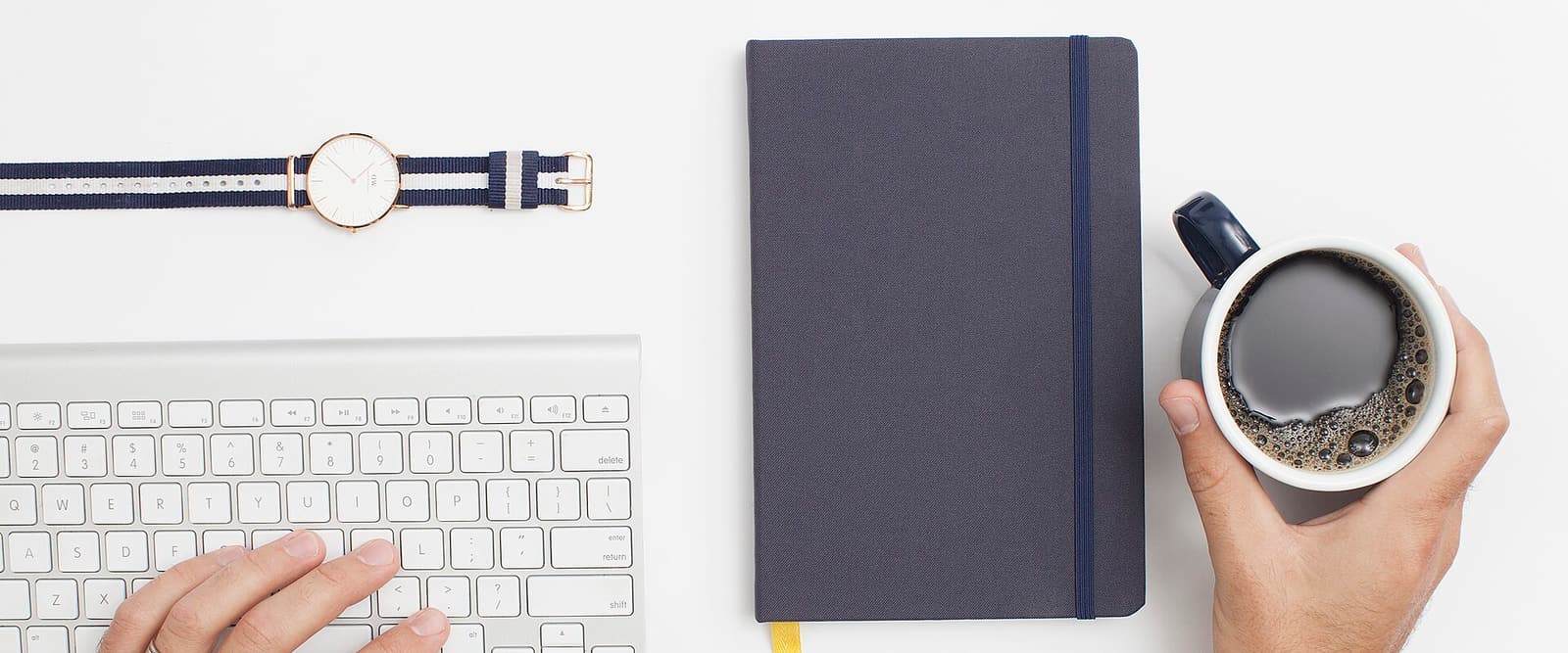 Notizbuch, Tastatur und eine Tasse Kaffee auf einem hellen Schreibtisch